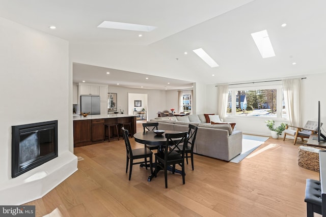 dining room featuring lofted ceiling with skylight, a glass covered fireplace, light wood finished floors, and recessed lighting