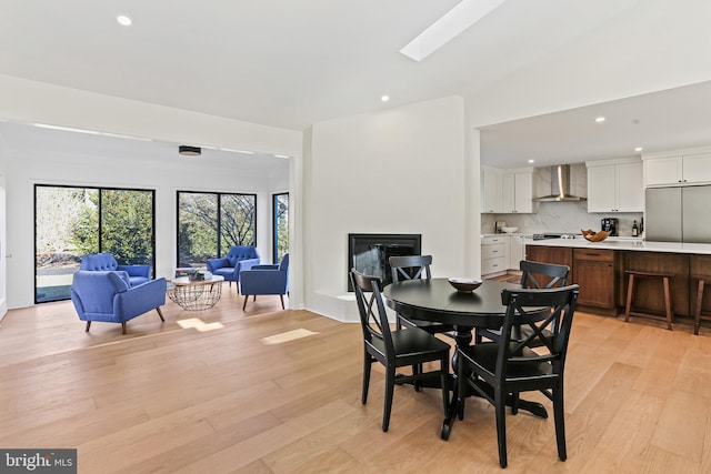 dining space with a glass covered fireplace, recessed lighting, light wood finished floors, and a skylight