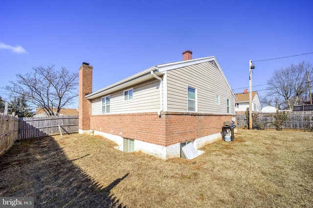 view of side of home featuring brick siding, a lawn, a chimney, and a fenced backyard