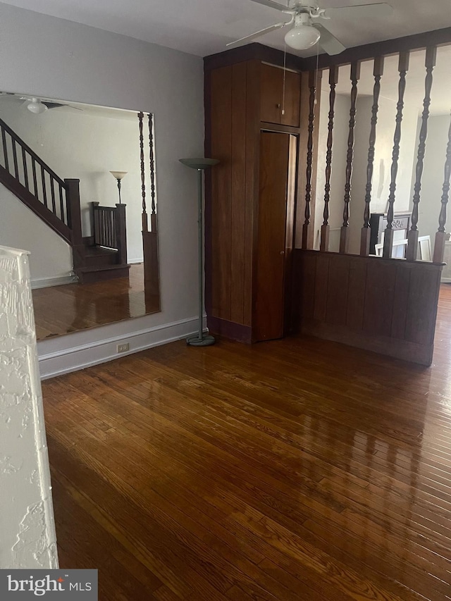 unfurnished living room with stairs, ceiling fan, wood finished floors, and baseboards