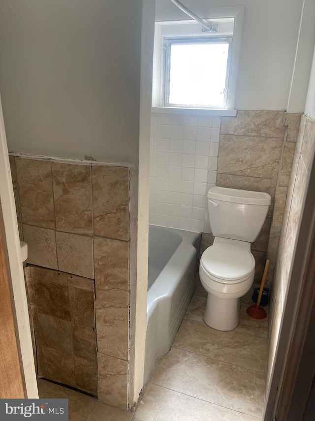 bathroom featuring toilet, a wainscoted wall, a bathing tub, and tile walls