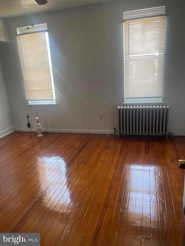 spare room with baseboards, hardwood / wood-style floors, and radiator heating unit