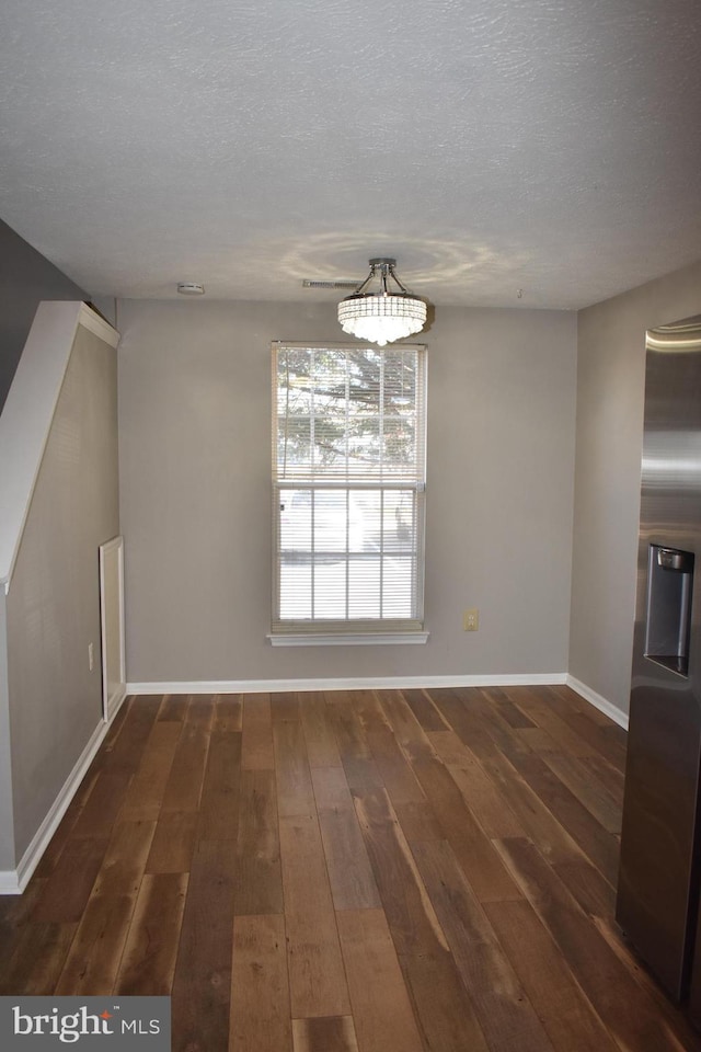 unfurnished dining area with a textured ceiling, dark wood-type flooring, and baseboards