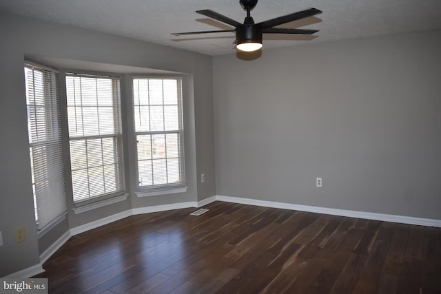 spare room with a ceiling fan, dark wood-style flooring, visible vents, and baseboards