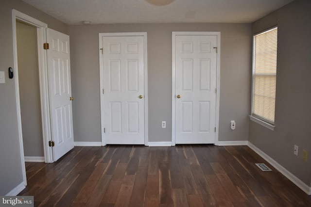 unfurnished bedroom with visible vents, dark wood finished floors, and baseboards