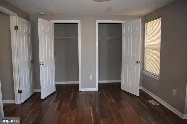 unfurnished bedroom with wood finished floors, visible vents, baseboards, multiple windows, and two closets