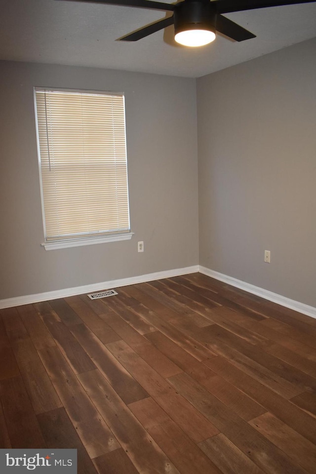 empty room with dark wood-style floors, baseboards, visible vents, and a ceiling fan