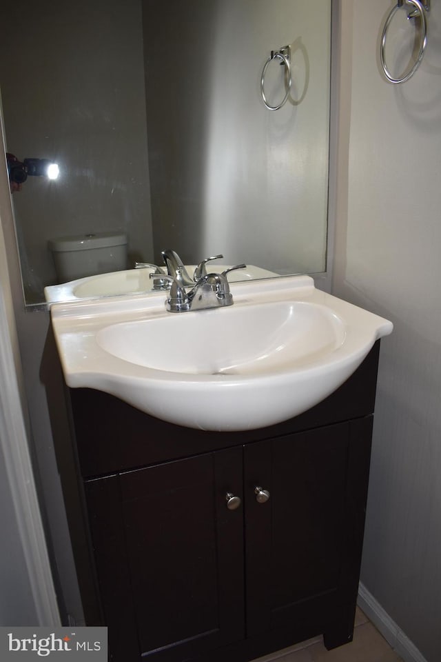 half bath with toilet, baseboards, and vanity