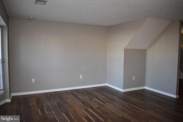 additional living space with visible vents, a textured ceiling, baseboards, and dark wood-type flooring