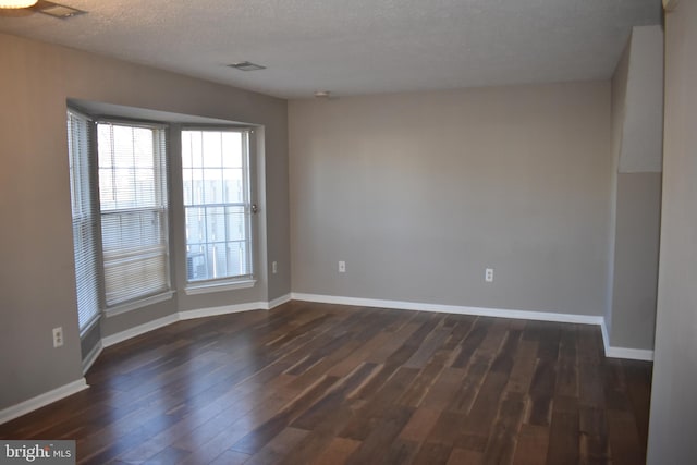 spare room with baseboards, a textured ceiling, visible vents, and dark wood-type flooring