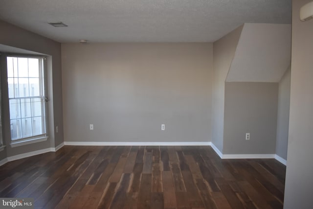 spare room featuring visible vents, dark wood finished floors, a textured ceiling, and baseboards