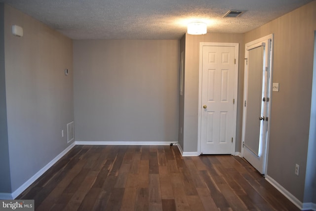 unfurnished room with a textured ceiling, dark wood-type flooring, visible vents, and baseboards