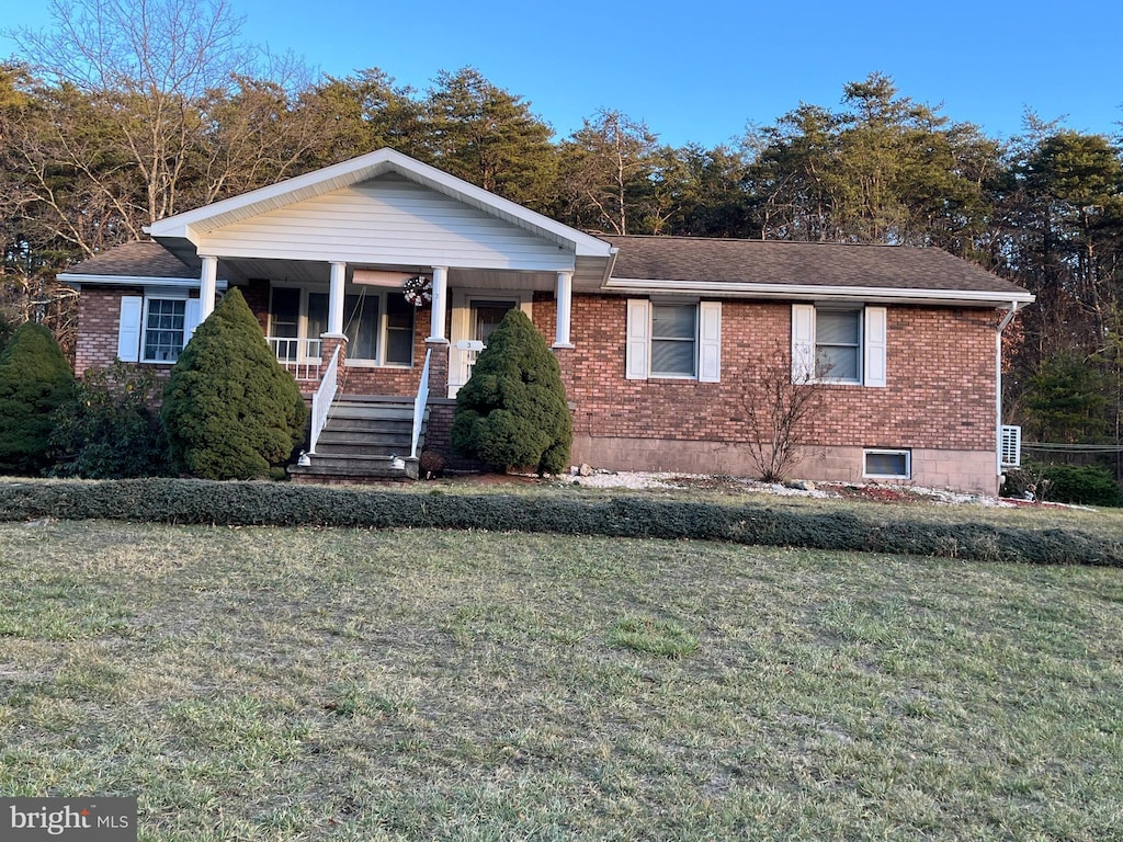 view of front of home with brick siding, a porch, a front yard, and a shingled roof