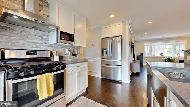 kitchen featuring stainless steel appliances, white cabinetry, ornamental molding, backsplash, and wall chimney exhaust hood