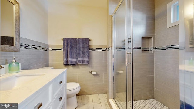 bathroom with toilet, a stall shower, vanity, and tile walls