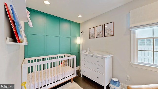 bedroom featuring a nursery area, dark wood-type flooring, multiple windows, and recessed lighting