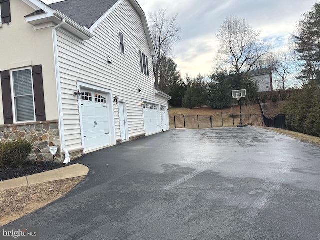 view of side of home with aphalt driveway, a shingled roof, fence, a garage, and stone siding