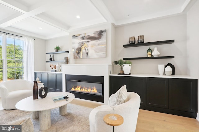 living area featuring beamed ceiling, coffered ceiling, light wood-type flooring, and a glass covered fireplace