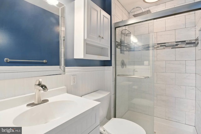 full bath featuring vanity, a shower stall, toilet, and a wainscoted wall