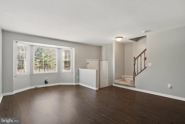 unfurnished living room featuring stairway, baseboards, and wood finished floors