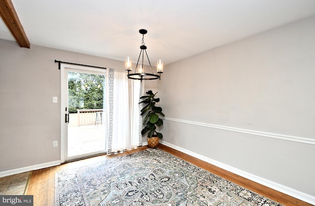 unfurnished dining area with a chandelier, wood finished floors, beam ceiling, and baseboards