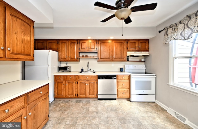 kitchen featuring white appliances, brown cabinets, light countertops, under cabinet range hood, and a sink