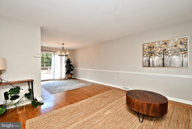 living area with baseboards, wood finished floors, visible vents, and a notable chandelier