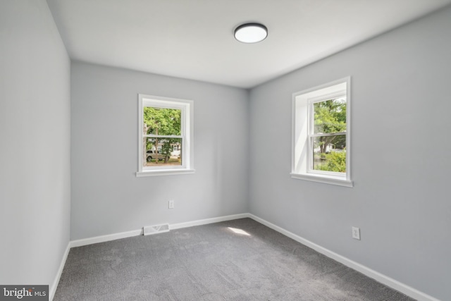 carpeted spare room featuring baseboards, visible vents, and a wealth of natural light