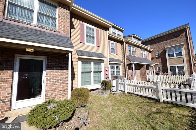 view of front of home featuring cooling unit, brick siding, fence, and roof with shingles