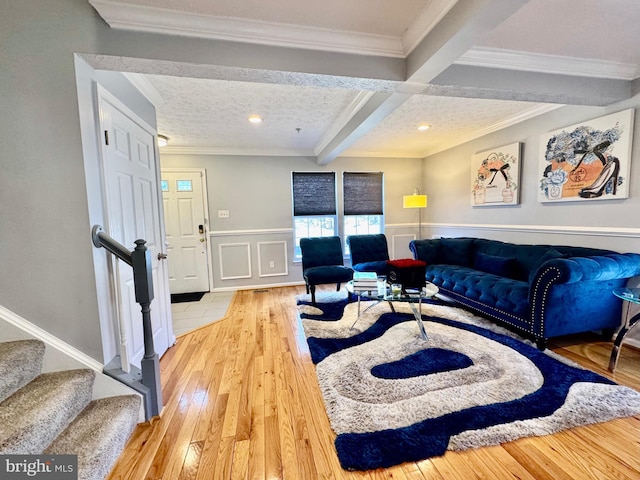 living area with a textured ceiling, wainscoting, beam ceiling, hardwood / wood-style floors, and crown molding