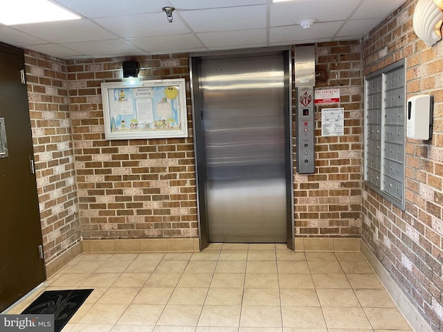 kitchen with elevator, brick wall, mail area, and a drop ceiling