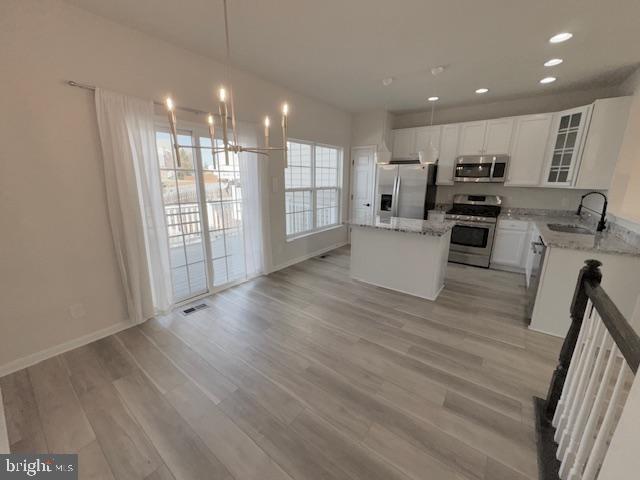kitchen featuring visible vents, a center island, stainless steel appliances, light wood-type flooring, and a sink