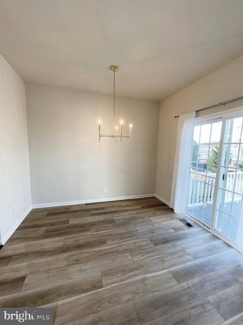 unfurnished dining area featuring visible vents, a notable chandelier, baseboards, and wood finished floors