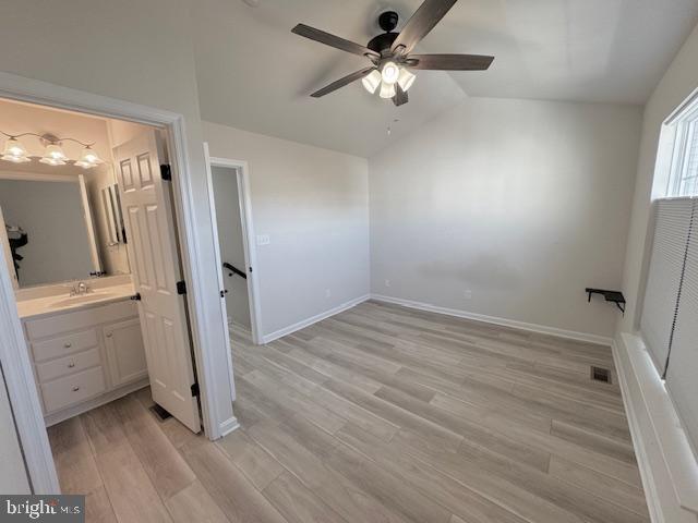 unfurnished bedroom with light wood-style floors, lofted ceiling, a sink, and baseboards