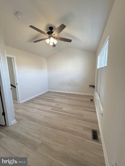 spare room with baseboards, visible vents, a ceiling fan, vaulted ceiling, and light wood-type flooring