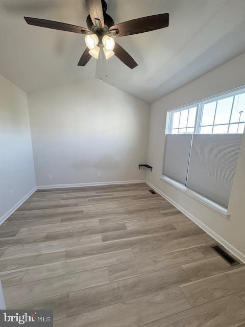 unfurnished room featuring lofted ceiling, light wood-type flooring, visible vents, and baseboards