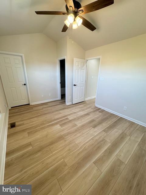 unfurnished bedroom with ceiling fan, visible vents, baseboards, vaulted ceiling, and light wood-style floors