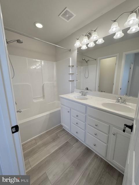 full bath featuring  shower combination, visible vents, a sink, and wood finished floors
