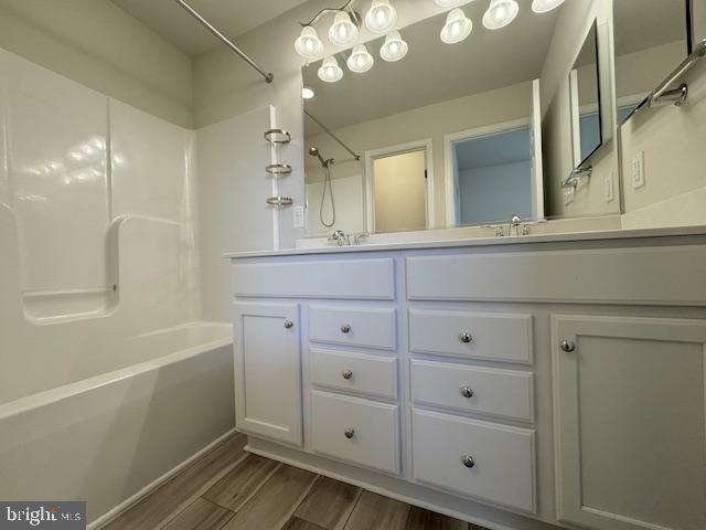 full bath featuring double vanity, tub / shower combination, a sink, and wood finished floors