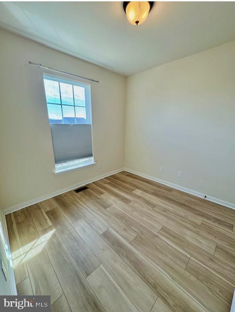 empty room featuring light wood-style floors, visible vents, and baseboards