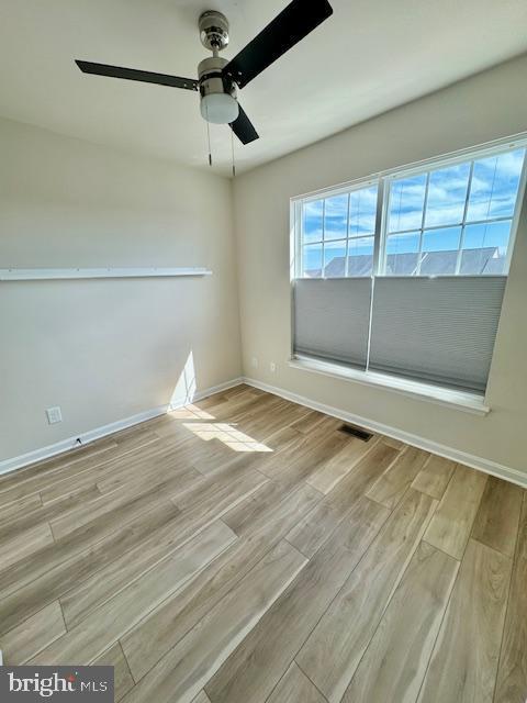 spare room with wood finished floors, visible vents, and baseboards