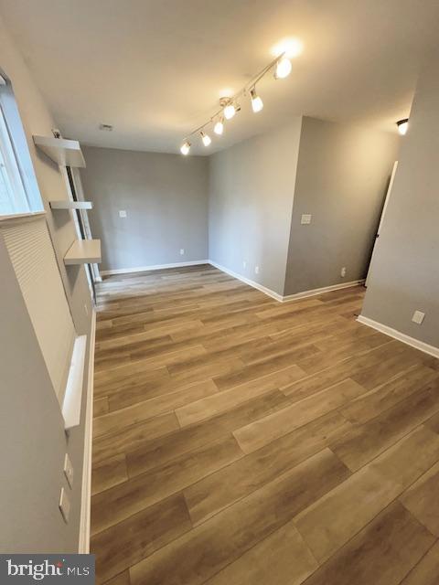 unfurnished living room featuring wood finished floors, rail lighting, and baseboards