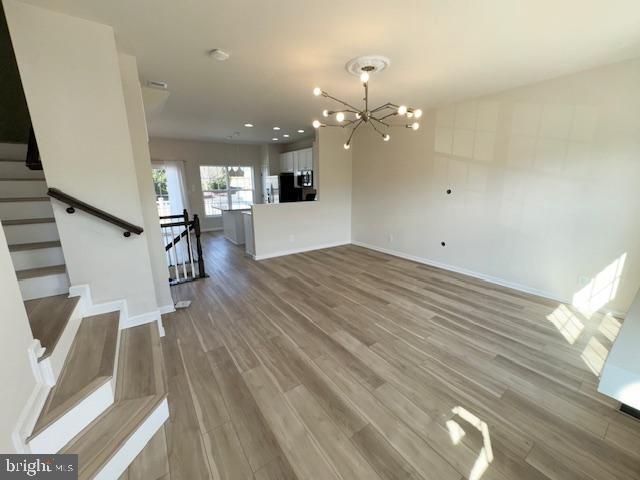 unfurnished living room with an inviting chandelier, stairs, baseboards, and wood finished floors
