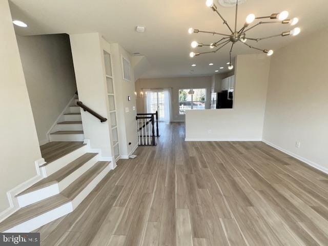 unfurnished living room with baseboards, stairway, an inviting chandelier, and wood finished floors