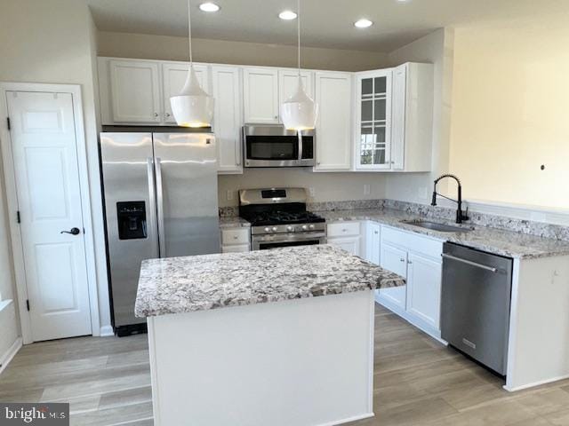 kitchen with light stone counters, a center island, stainless steel appliances, light wood-type flooring, and a sink