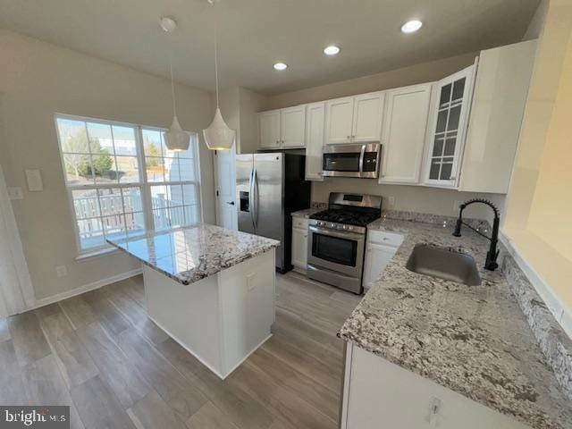 kitchen with a center island, stainless steel appliances, white cabinets, a sink, and light stone countertops