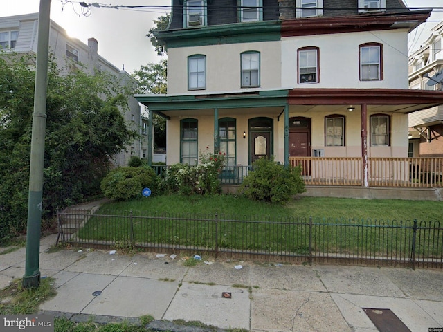 second empire-style home with mansard roof, a fenced front yard, covered porch, stucco siding, and a front yard