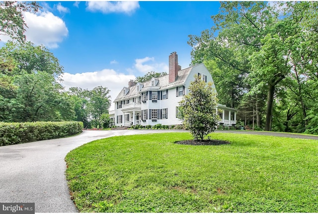 view of front of house with aphalt driveway, a chimney, a front lawn, and a gambrel roof