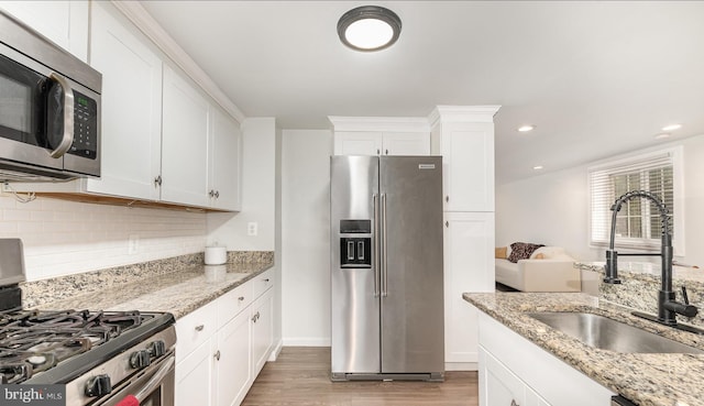 kitchen with stainless steel appliances, backsplash, light wood-style flooring, white cabinetry, and a sink