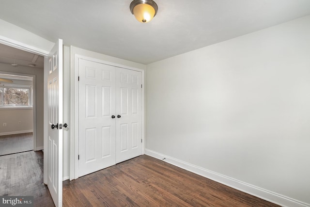 unfurnished bedroom with dark wood-type flooring, a closet, and baseboards